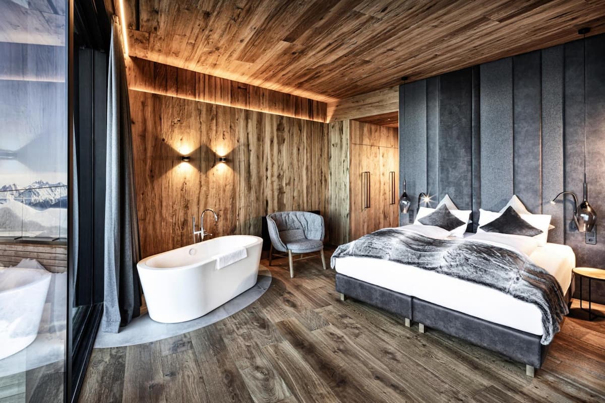 A modern bedroom with a large bed, a bathtub, and a chair.