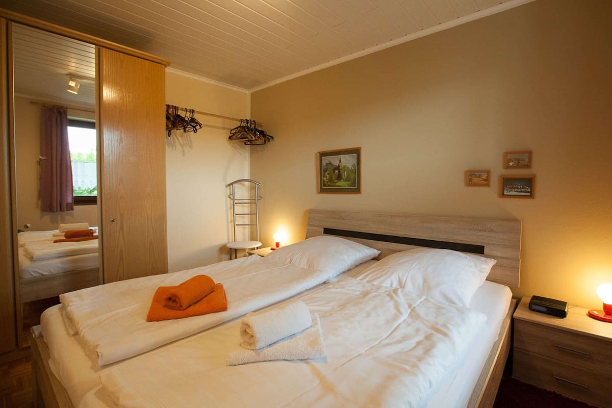Una habitación de hotel con cama, mesita de noche, lámpara, espejo y armario.