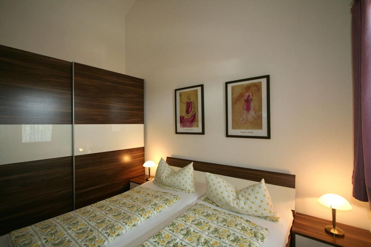Una cama doble con ropa de cama floral, dos lámparas de noche y dos cuadros en la pared.