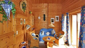 A cozy wooden cabin interior with a blue sofa, wicker chairs, a small round table, and a hanging light fixture. - Holiday Homes Lauterdorfle, Hayingen (Hayingen)