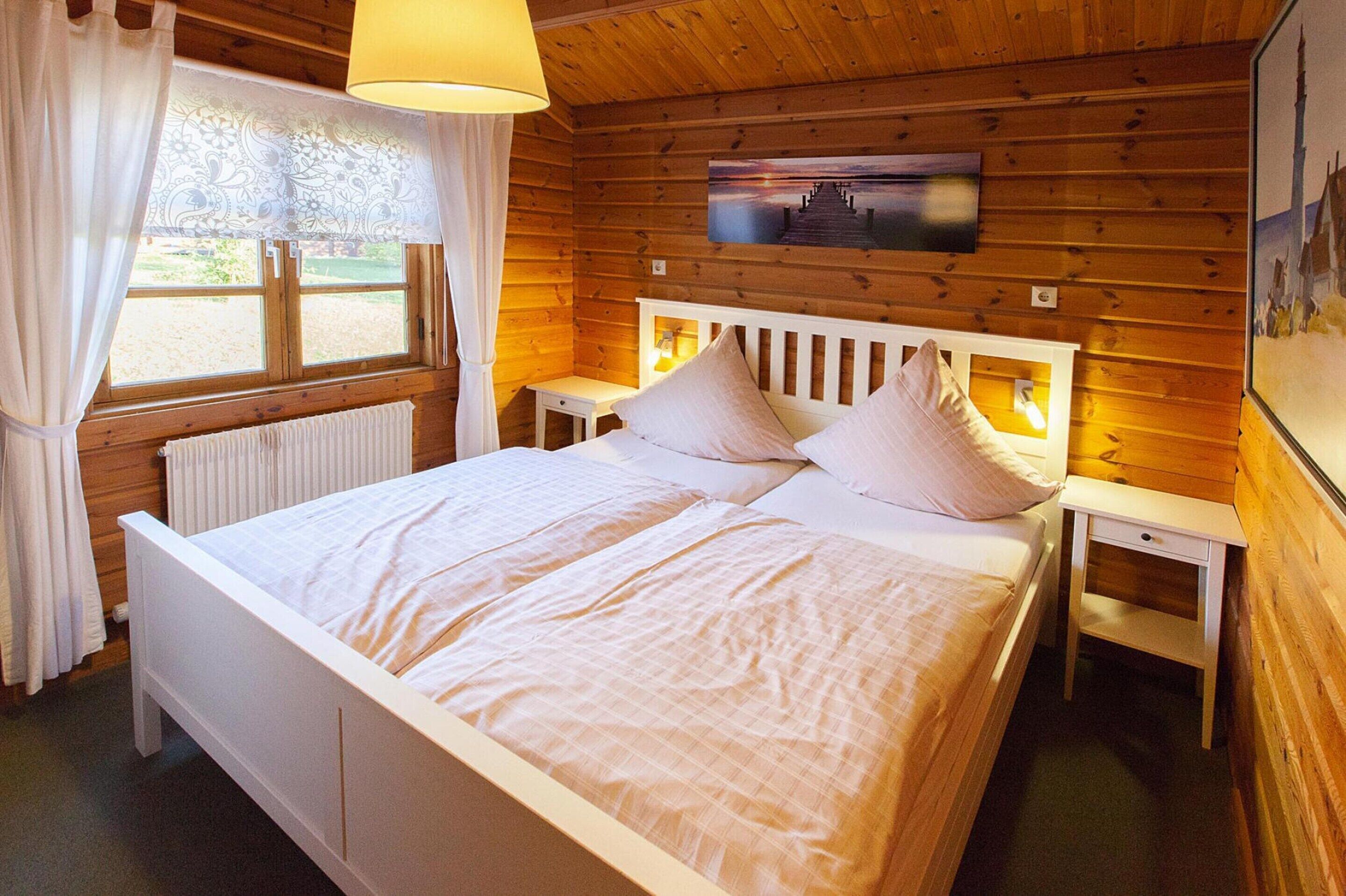 Een slaapkamer met houten lambrisering, een bed, nachtkastjes en een raam met gordijnen.