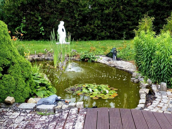A garden with a pond, a statue, and a wooden deck. - Cottages by the Pond, Zinnowitz (Zinnowitz)