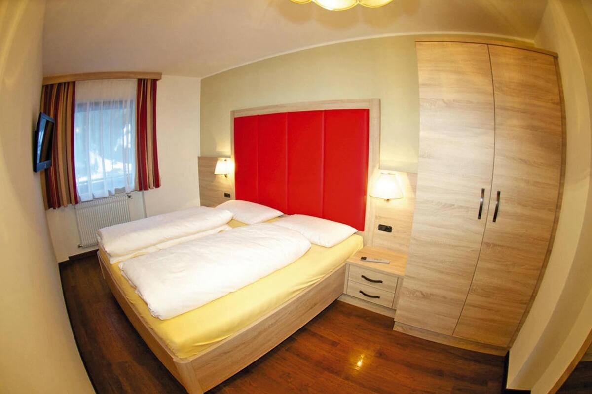 A hotel room with a large bed, wooden wardrobe, bedside lamps, and a TV mounted on the wall.