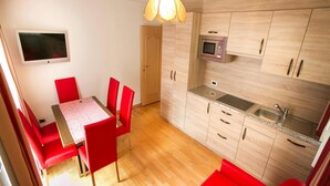 Una cucina compatta con mobili in legno, un forno a microonde e un lavello. È presente una zona pranzo con un tavolo e sedie rosse.