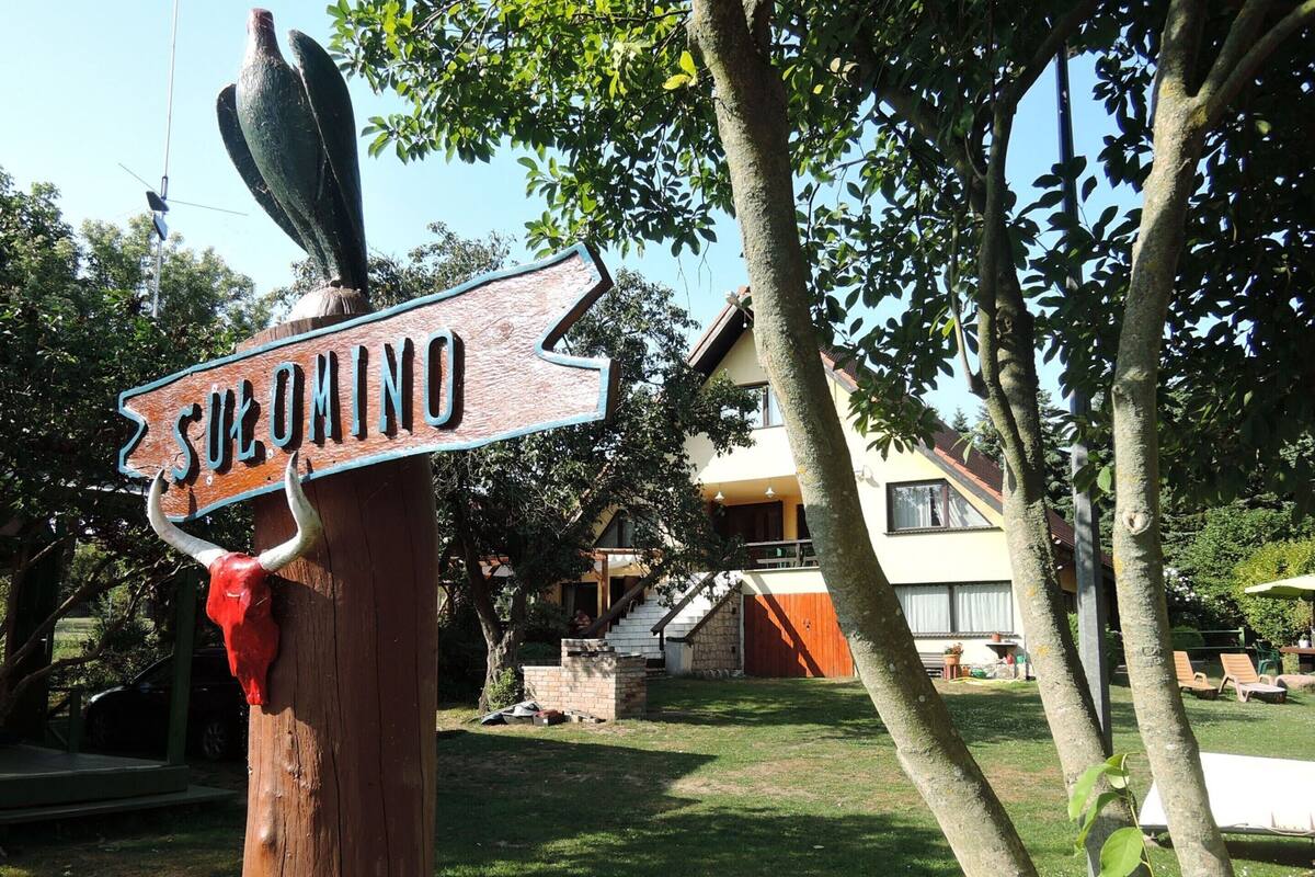 A wooden signpost with 'SILVANO' written on it, pointing to a house with a balcony and a staircase leading to the entrance.