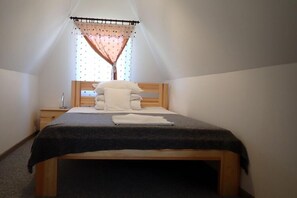 A small, single-bed room with a wooden headboard, a bedside table, and a window with a curtain. - Bungalow in Kolczewo With Parking Space (gmina Wolin)