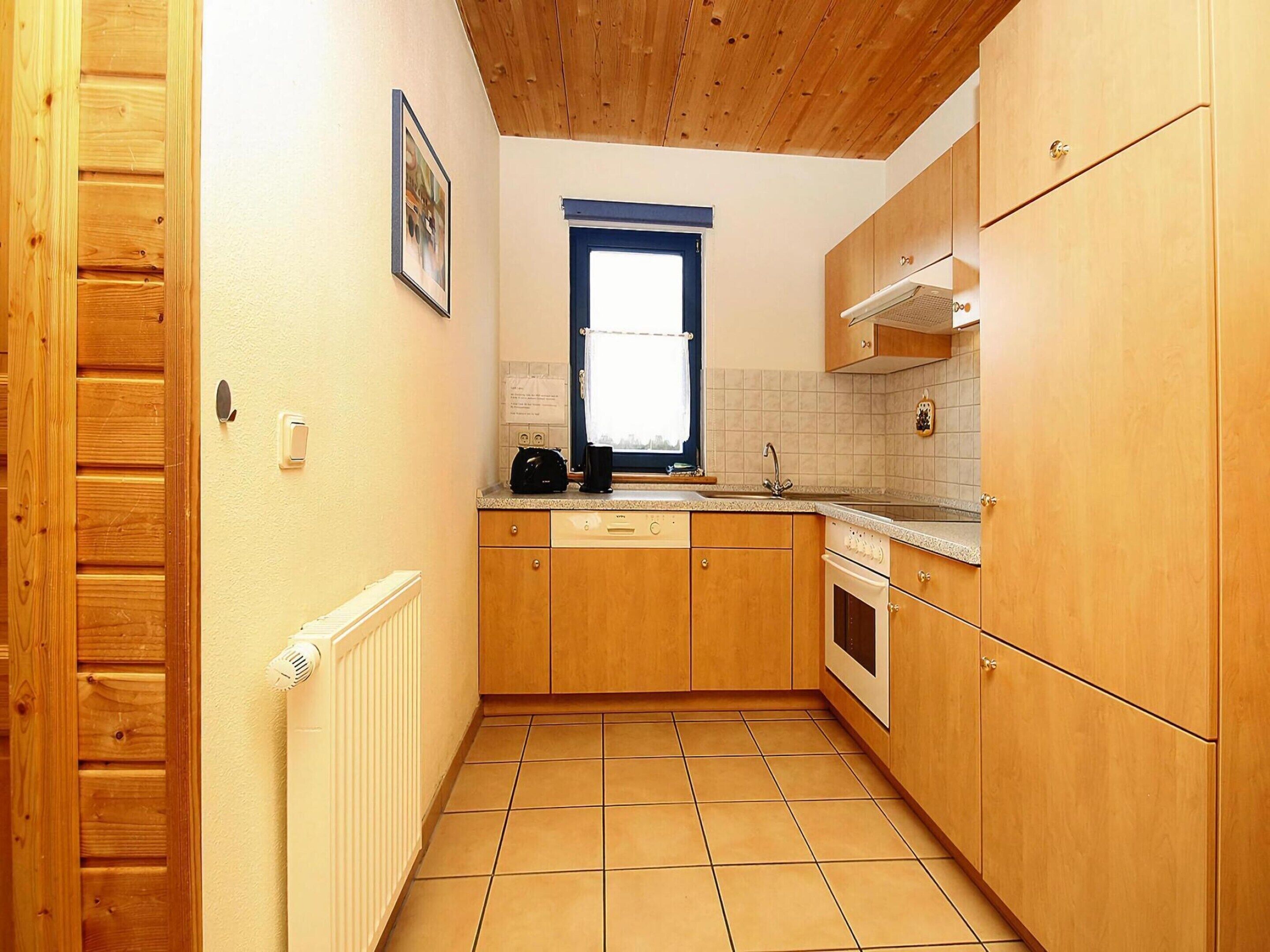 A compact kitchen with wooden cabinets, a built-in oven, a window with a view, and a radiator.