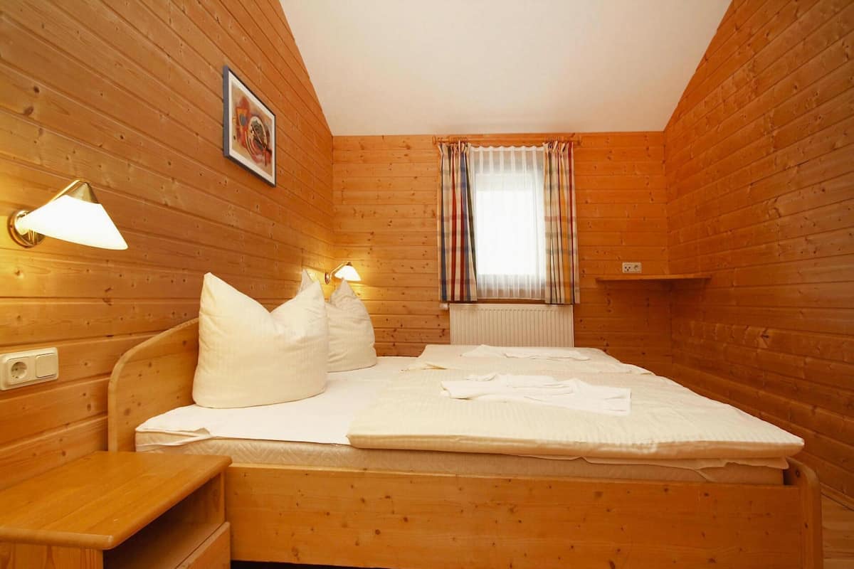 Une pièce aux murs lambrés, comprenant un lit, des lampes de chevet, une fenêtre avec des rideaux et un tableau accroché au mur.