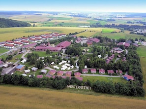 An aerial view of Westerstadt with multiple buildings, including residential houses and a large complex with red roofs. - Ferienpark Harz in Hasselfelde (Oberharz am Brocken)