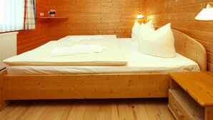 A wooden bed with a mattress, pillows, and a bedside table in a room with wooden walls and flooring. - Ferienpark Harz in Hasselfelde (Oberharz am Brocken)