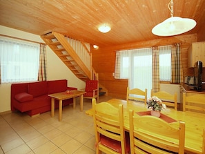 A wooden cabin interior with a sofa, dining table, chairs, a staircase, and a kitchen area. - Ferienpark Harz in Hasselfelde (Oberharz am Brocken)