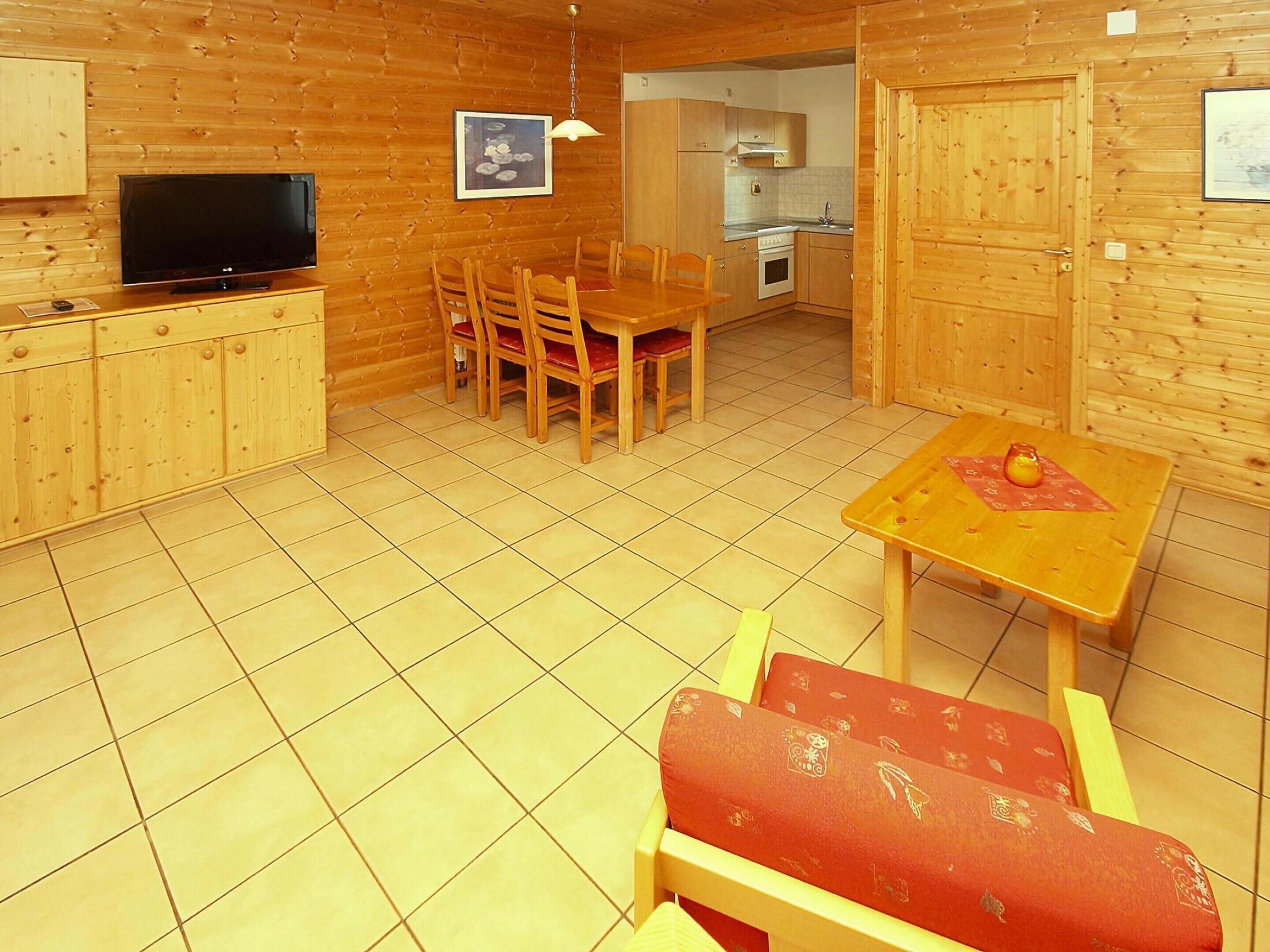 A wooden interior with a TV, dining table, chairs, and a kitchen area.