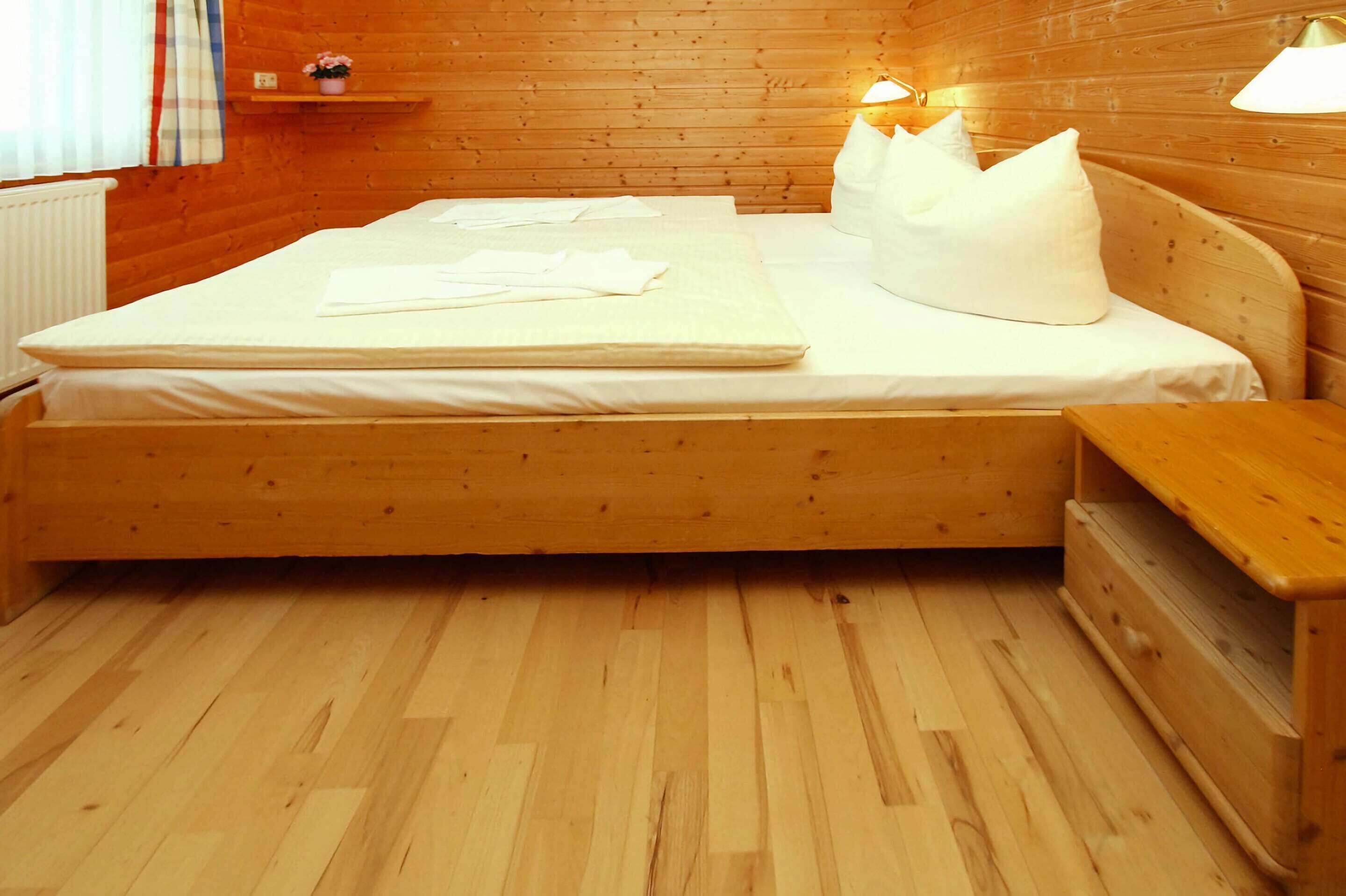 Un lit en bois avec une literie blanche, une table de chevet et une petite table à poser près du lit.