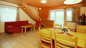 A wooden interior with a sofa, dining table, chairs, a staircase, and a kitchen area. - Ferienpark Harz in Hasselfelde (Oberharz am Brocken)