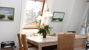 Un comedor con una mesa, sillas de mimbre, un florero con flores y un radio sobre un soporte.