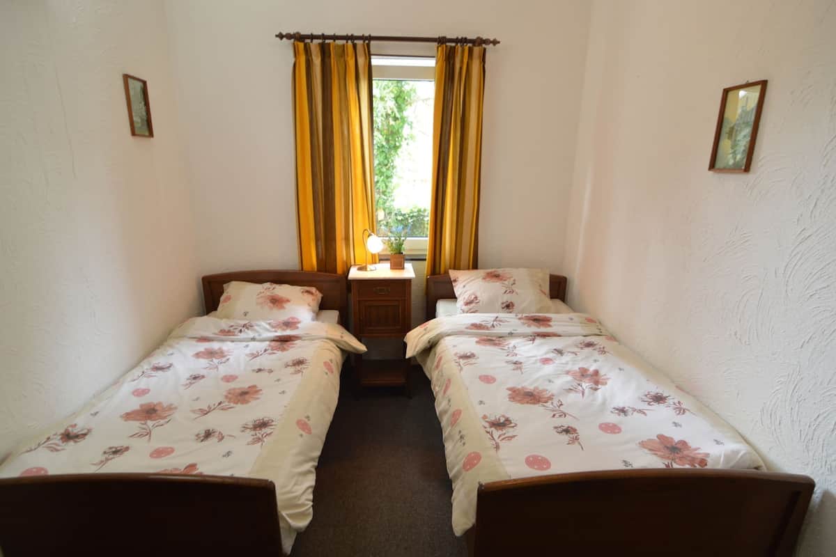 Een kamer met twee éénpersoonsbedden, een nachtkastje met een lamp en een raam met gordijnen.