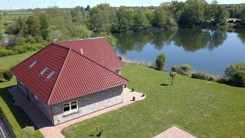 A house with a red roof, a stone base, and a pond in the background.