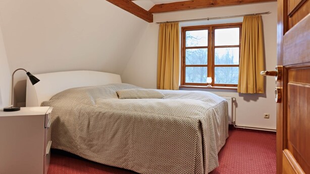 A bedroom with a bed, a desk with a lamp, a window with curtains, and wooden beams on the ceiling. - Holiday House Monika, Wendorf (Kuhlen-Wendorf)
