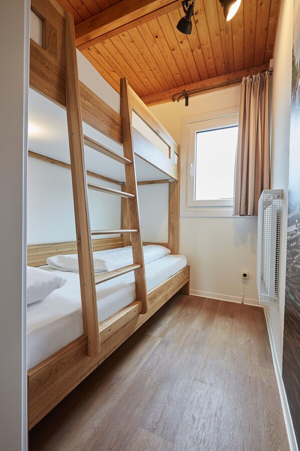 Une chambre avec un lit superposé, des poutres en bois, une fenêtre avec des rideaux et un ventilateur fixé au mur.