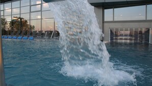 Une piscine dans laquelle de l’eau jaillit d’une structure surplombante, le tout entouré d’un bâtiment moderne doté de grandes fenêtres.