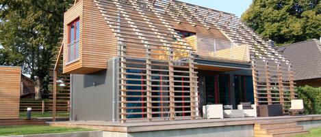 A modern house with a sloped roof, a wooden deck, and a small outdoor seating area.