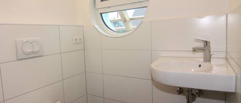 Une petite salle de bain propre, équipée de toilettes, d’un lavabo et d’une fenêtre.