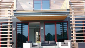 Ein modernes Haus mit einer Holterrasse, zwei Korbschaukeln mit Kissen und einem Glastür-Eingang.
