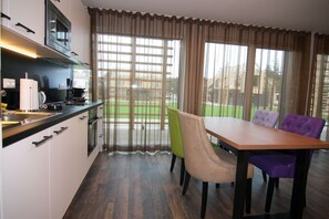 Una cocina moderna con zona de comedor, que cuenta con una mesa y sillas de madera, un ventanal con cortinas y vistas a un paisaje verde.