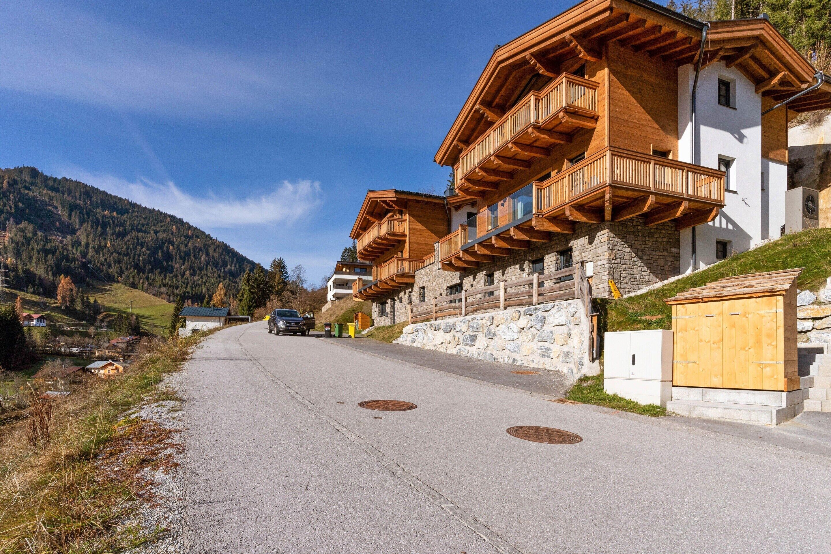 A row of wooden chalet-style buildings with balconies, a stone wall, and a clear sky.
