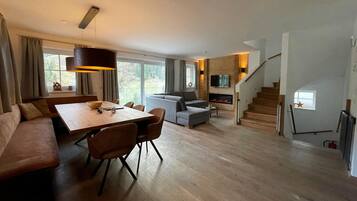 A modern living room with a wooden dining table, grey sofa, and a staircase leading to a loft area.