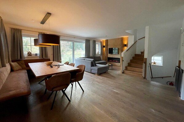 Un salon moderne avec une table à manger en bois, un canapé gris et un escalier menant à une mezzanine.
