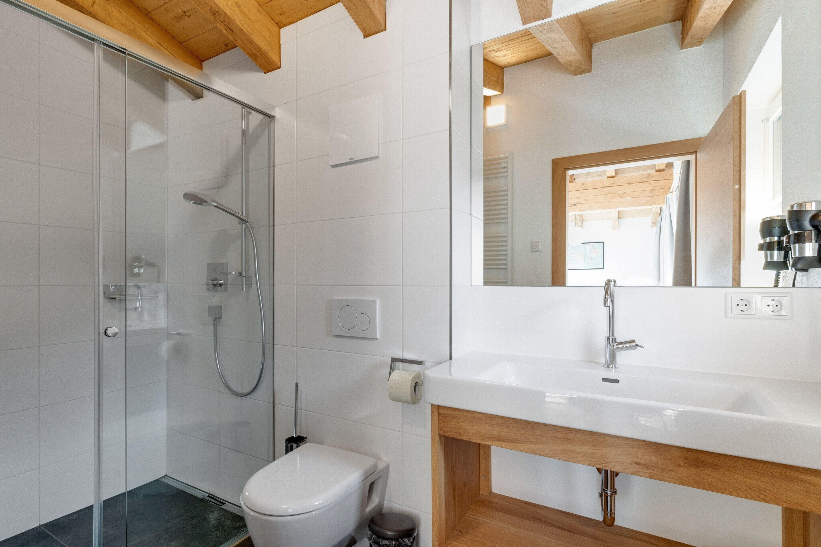A bathroom with a glass shower enclosure, a white toilet, a wooden vanity with a sink, and a mirror.