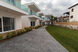 Un immeuble résidentiel moderne doté d’un chemin piétonnier pavé, d’une pelouse et d’une clôture en bois.