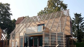 Una casa moderna con techo inclinado, ventanas grandes y una terraza de madera.