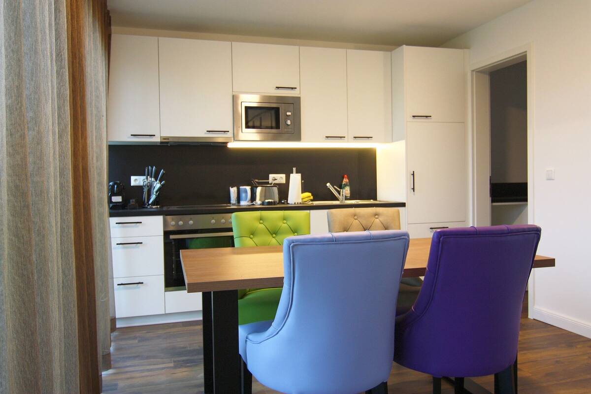 A modern kitchen with white cabinets, a microwave, and a dining area with two chairs.