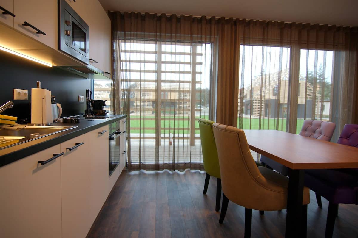 A modern kitchen with a dining area, large windows, and a view of the outdoors.