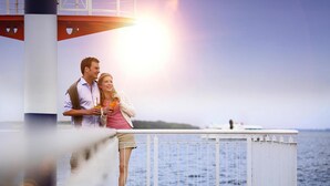 Ein Paar steht an einer Pier, im Hintergrund ist ein Leuchtturm zu sehen.