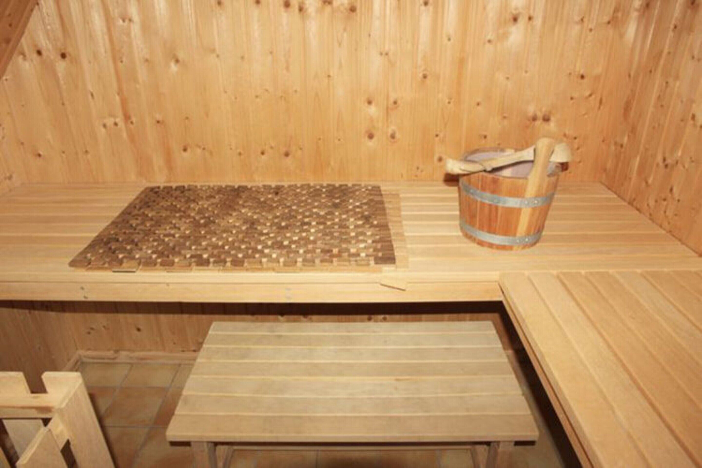 A wooden sauna room with a bench, a wooden bucket, and a mat on the floor.
