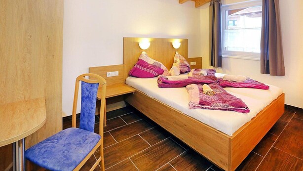 A small, cozy room with a wooden bed, a chair, and a nightstand. - Terraced Houses Oliver, Langenfeld (Laengenfeld)