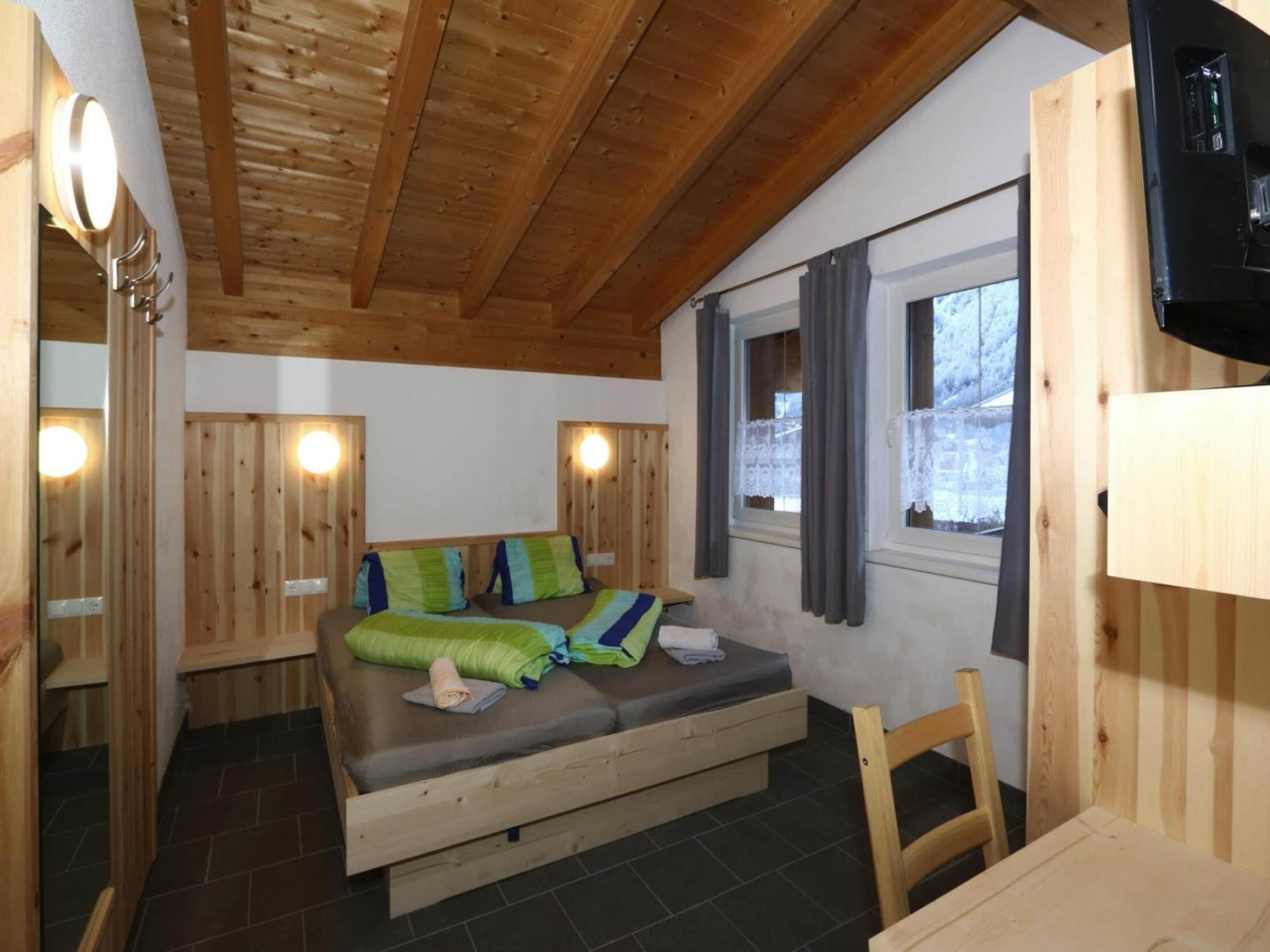 A wooden cabin room with a bed, a small table, and a TV.