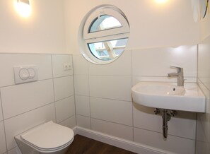 A small, modern bathroom with white tiles, a round window, a white sink, and a toilet. - Chalet, Wendorf (Kuhlen-Wendorf)