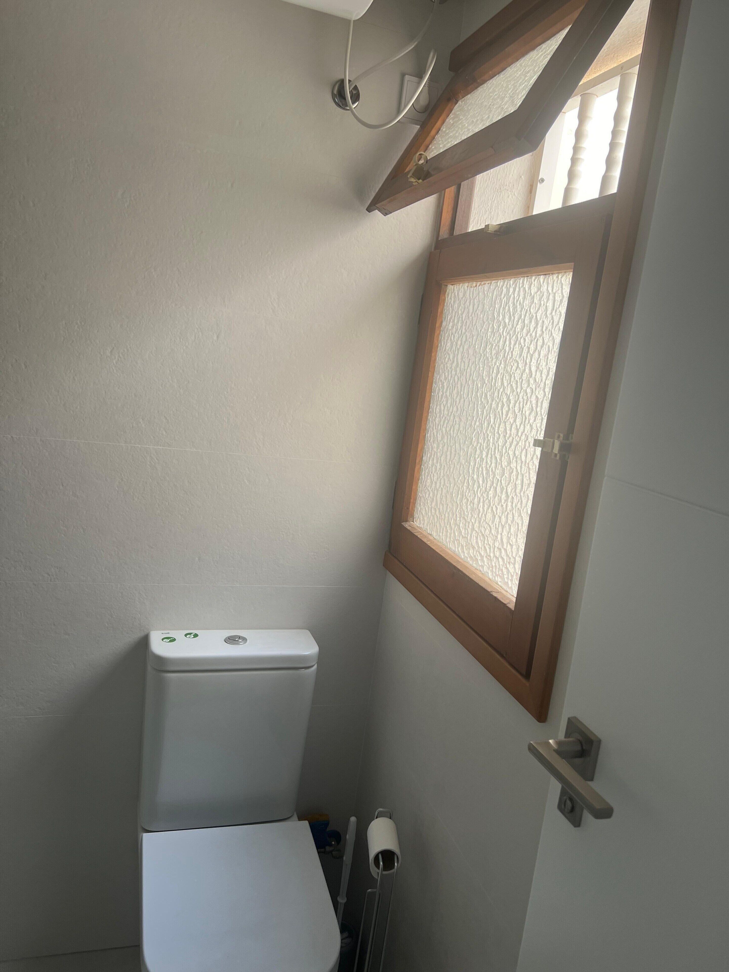 A small bathroom with a toilet, a window, and a towel rack.