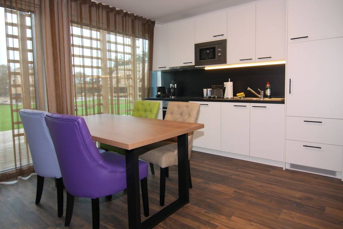 A modern kitchen with white cabinets, a wooden dining table, and purple chairs.