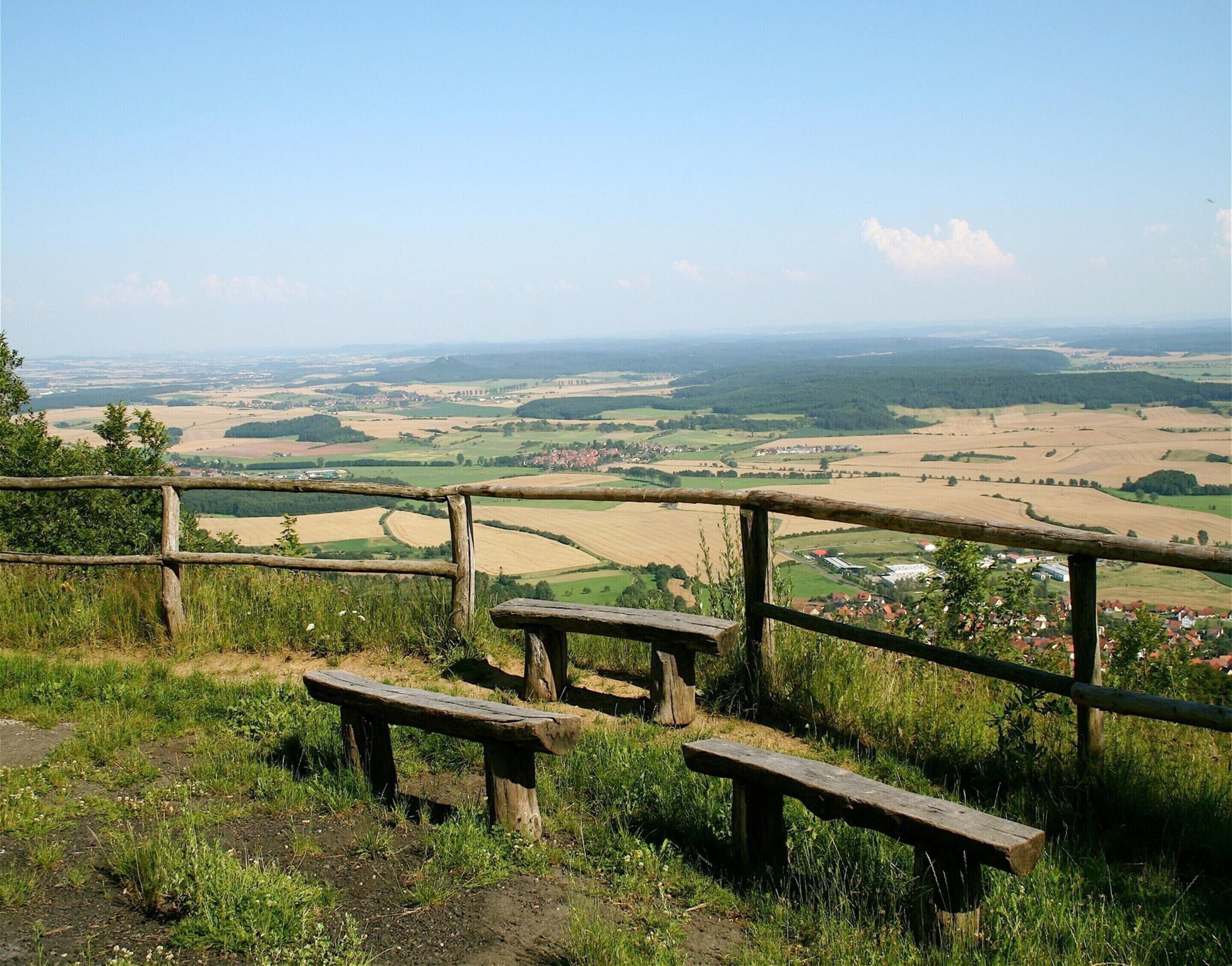 A wooden bench and railing overlooking a rural landscape with fields and distant buildings.