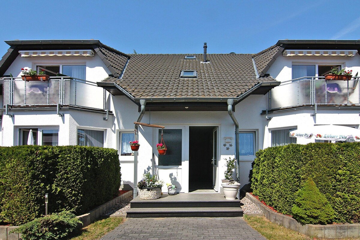 Een gebouw met twee verdiepingen, een pannendak, een centrale ingang en een klein balkon op de bovenverdieping.