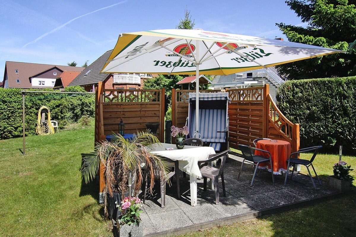 Een klein terras buiten, met een tafel, stoelen, een barbecue en een grote parasol.
