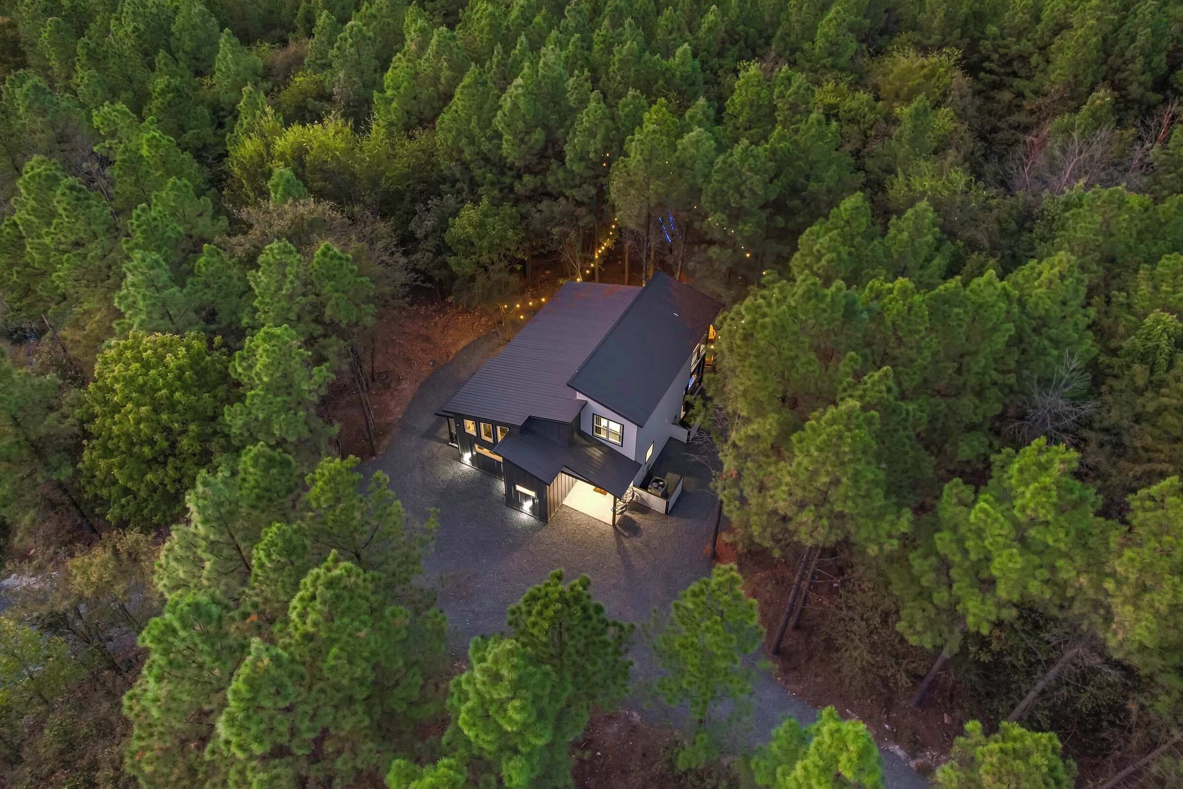 Une vue aérienne d’une maison entourée d’une forêt dense, avec une allée pavée menant à l’entrée.