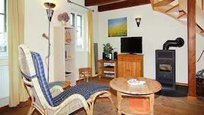 Una sala de estar acogedora con techo de madera, una mecedora de mimbre, una mesita, un televisor, una chimenea y una estantería.