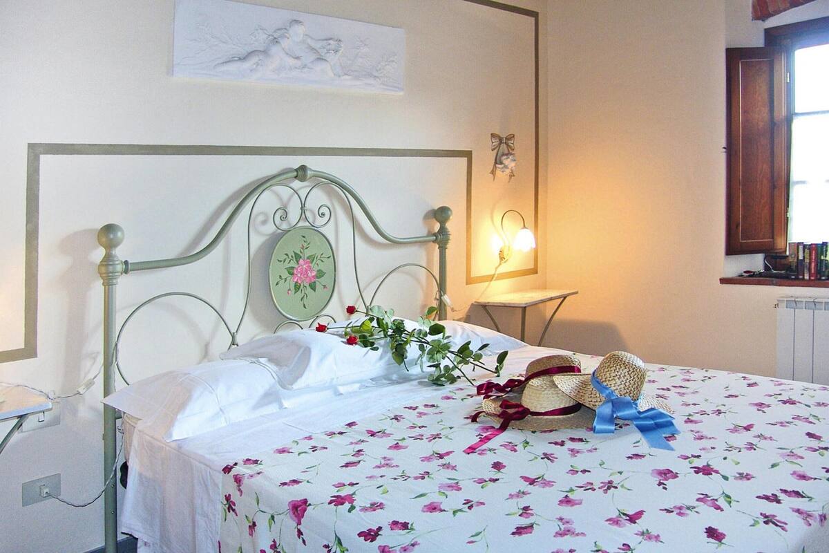 Una cama bien hecha con una colcha estampada con motivos florales, un cabecero decorativo y una lámpara de noche.