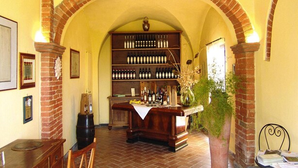 A wine cellar with brick arches, wooden shelves stocked with wine bottles, a bar area, and a dining table with chairs. - Agriturismo Poggio al Sole, Vinci (Vinci)